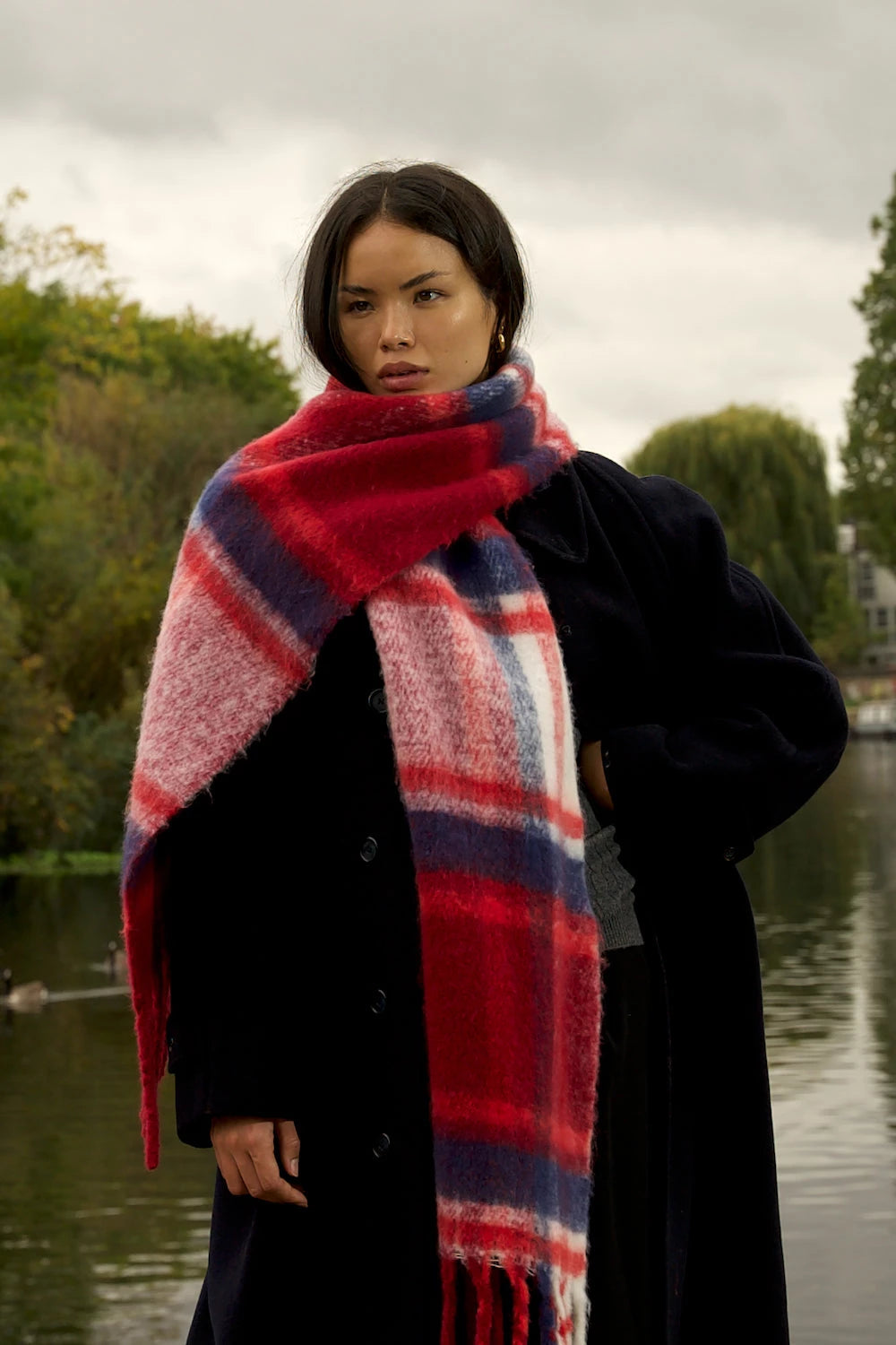 woman wearing oversized red & navy plaid scarf in front of canal