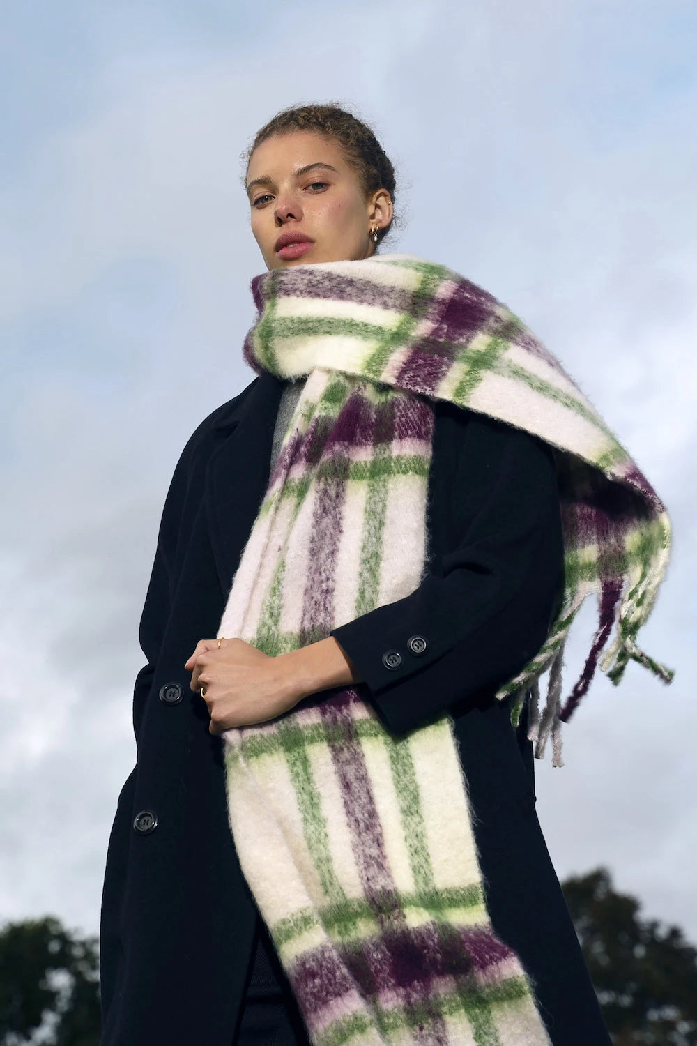 woman wearing oversized plaid scarf in winter with a sky background