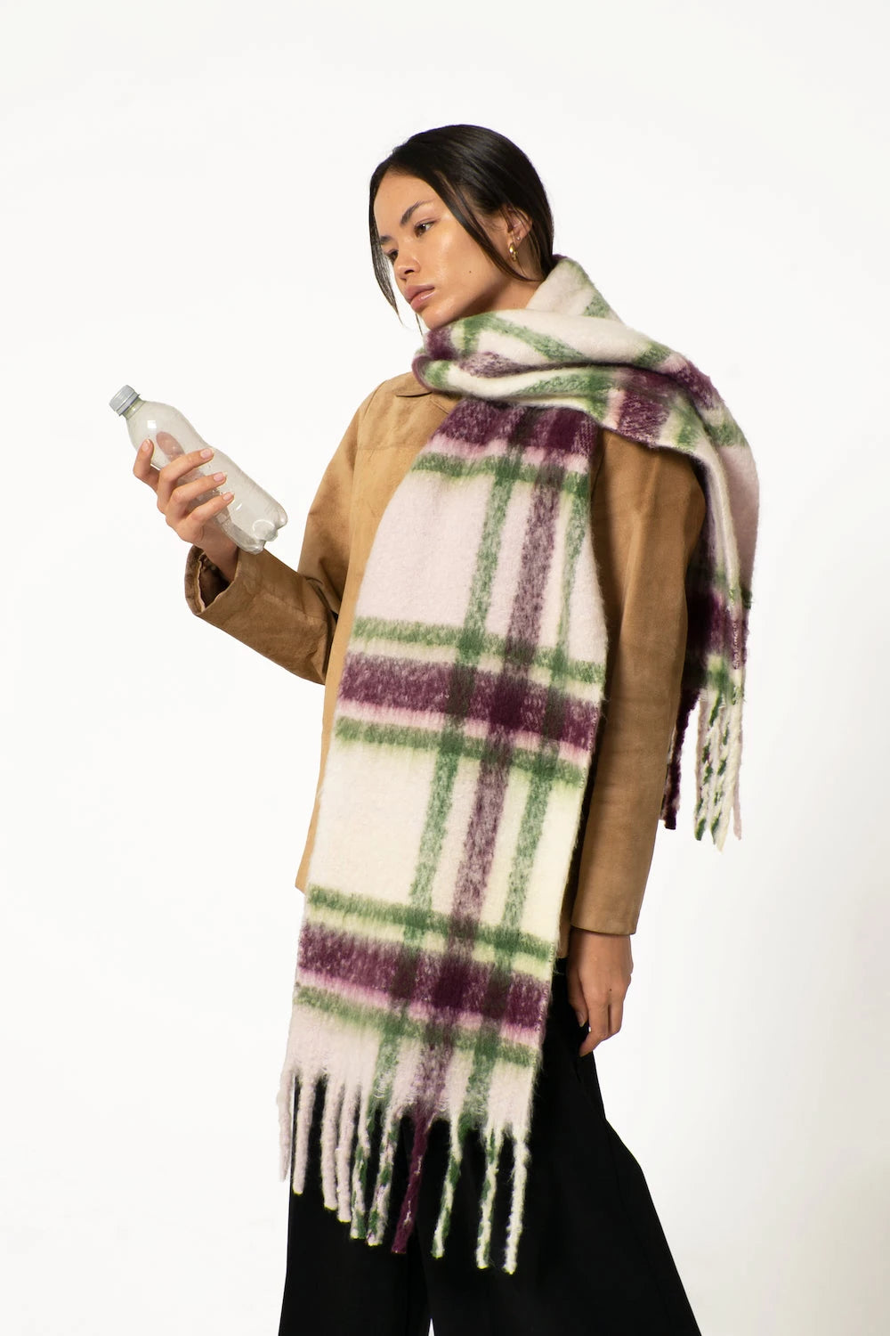 woman wearing oversized tasselled scarf, holding a plastic bottle